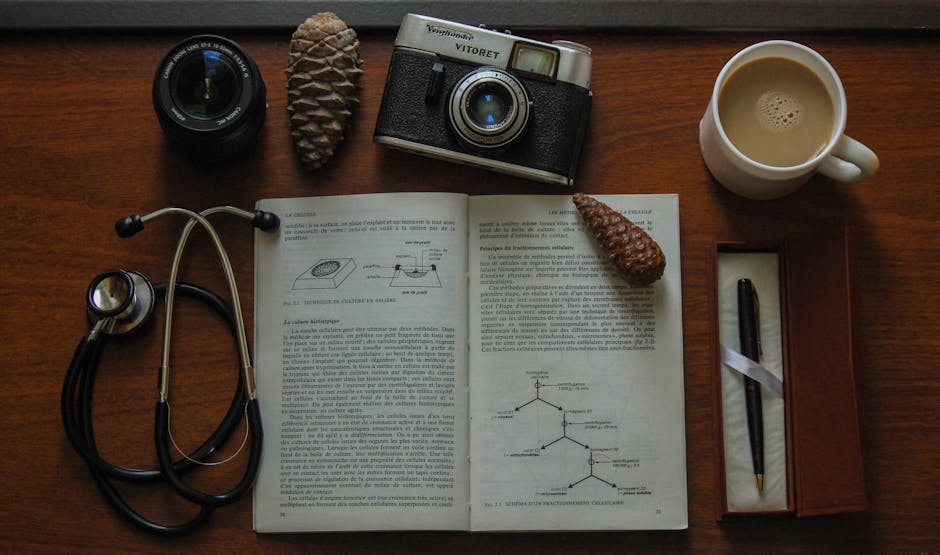 Top view of a vintage camera, open book, stethoscope, and coffee on a wooden table.